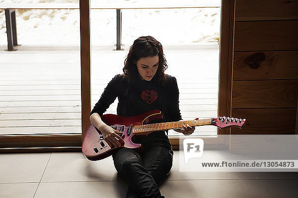 Teenager-Mädchen spielt Gitarre  während sie zu Hause auf dem Boden sitzt