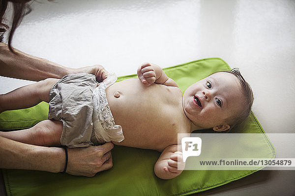 Portrait of cute baby girl lying on mat while mother changing diaper at home