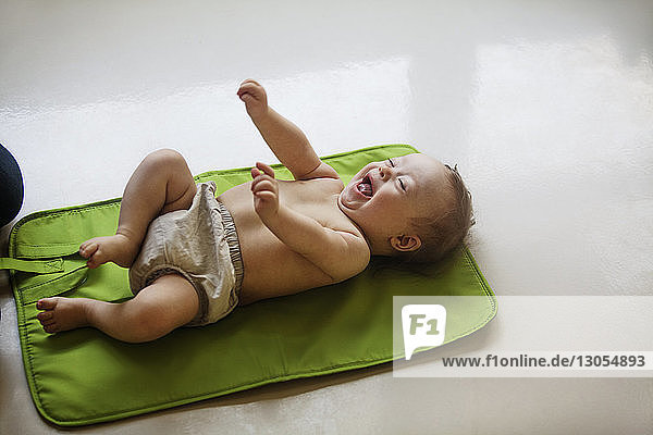 Baby girl laughing while lying on mat by mother at home