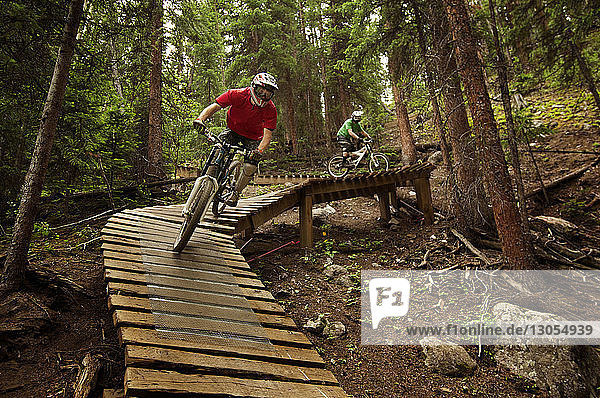 Cyclists cycling on sports ramp amidst trees in forest