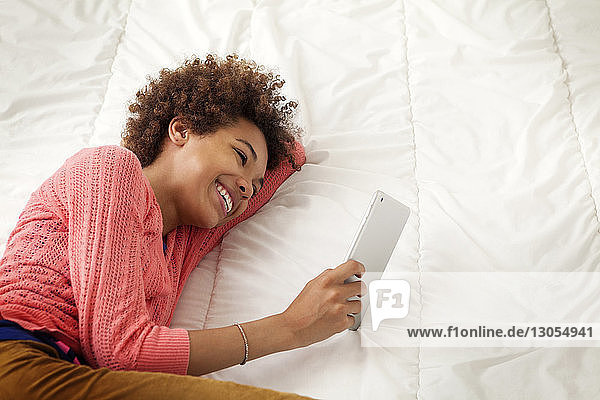 Happy girl holding tablet computer while lying on bed at home
