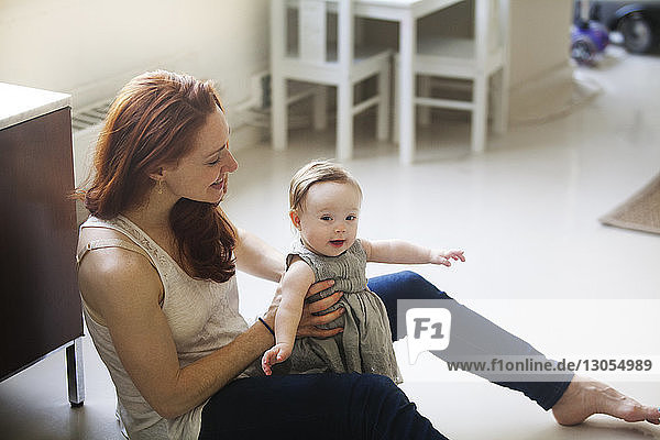 Mother holding daughter while sitting on floor at home