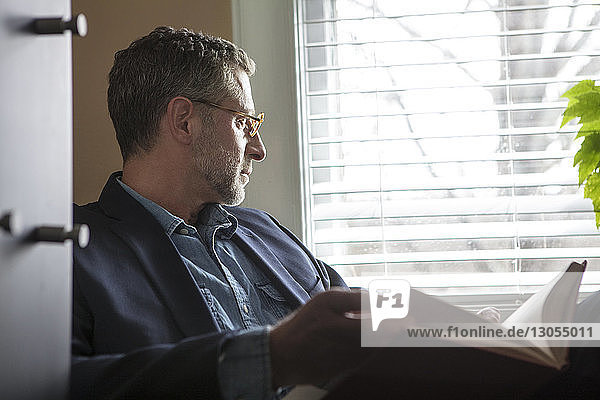 Man looking away while sitting by window at home