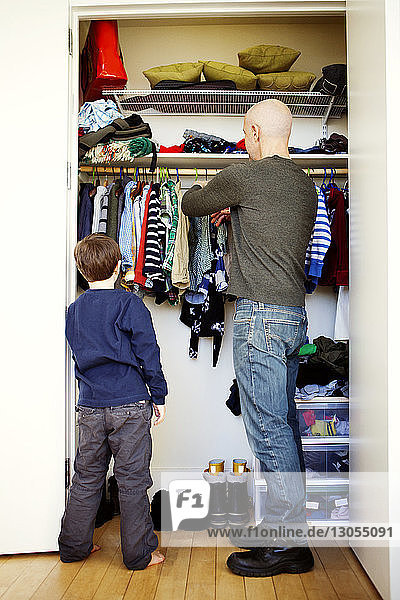 Junge steht mit Vater und zieht Kleider aus dem Schrank