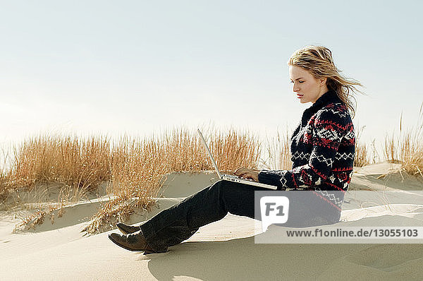 Frau benutzt Laptop-Computer  während sie auf Sand sitzt