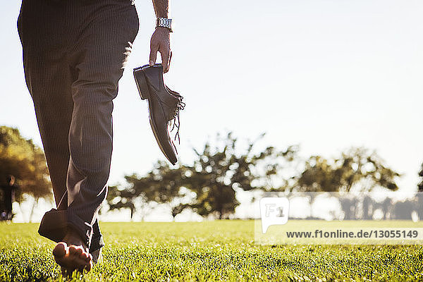 Niedriger Teil eines Mannes  der Schuhe hält und auf einem Grasfeld geht