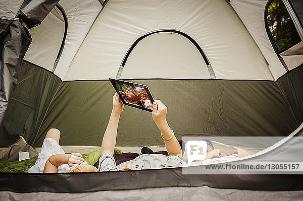 Bruder hält digitales Tablett  während er sich mit Schwestern im Zelt entspannt