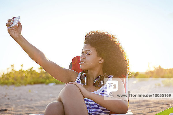 Woman taking through smart phone while relaxing at beach on sunny day