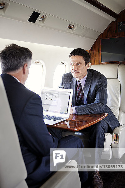 Businessman looking at partner using laptop in corporate jet