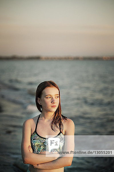 Nachdenkliches Mädchen schaut weg  während es bei Sonnenuntergang am Meer steht