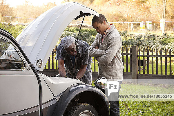 Älterer Mann repariert Auto nach Sohn auf Grasfeld stehend