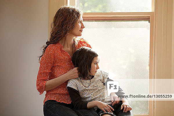 Mutter und Tochter schauen durchs Fenster  während sie zu Hause sitzen