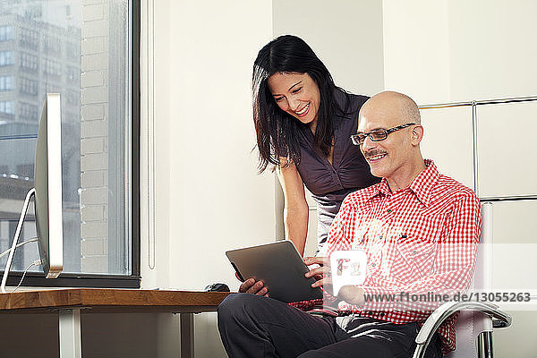 Happy businessman showing tablet computer to colleague at office