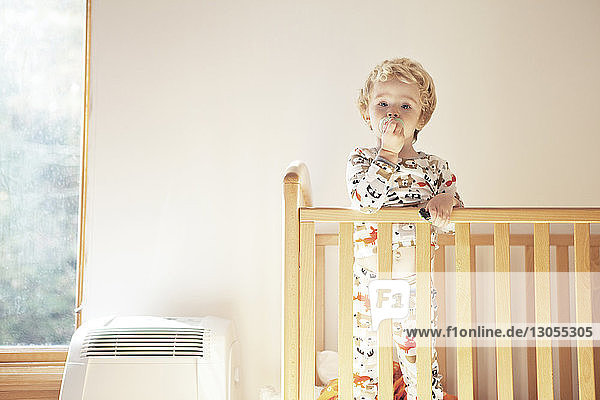 Portrait of cute boy standing in crib at home