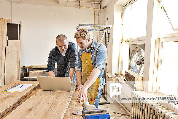 Male carpenters looking at laptop and discussing in workshop