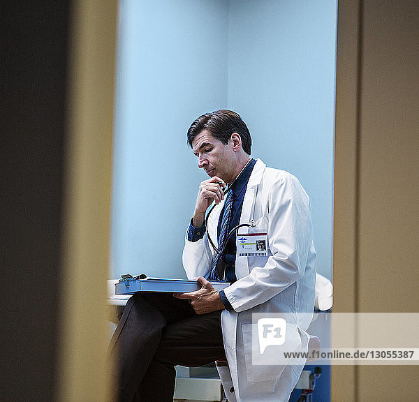 Nachdenklicher Arzt liest Dokumente  während er im Krankenhaus sitzt
