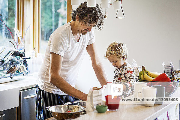 Father working while son sitting on kitchen worktop