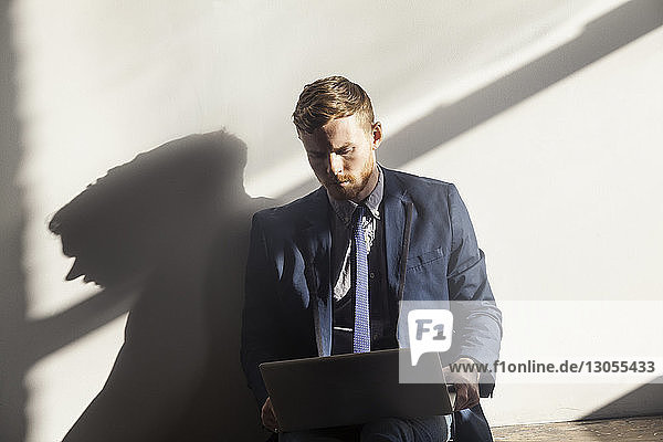 Man using laptop computer while sitting against wall at home