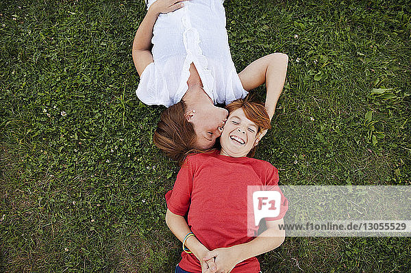 Draufsicht einer glücklichen Mutter  die ihren Sohn küsst  während er auf dem Feld liegt