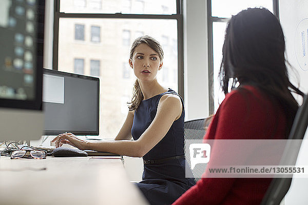 Geschäftsfrau schaut ihren Kollegen an  während sie am Computer am Schreibtisch arbeitet