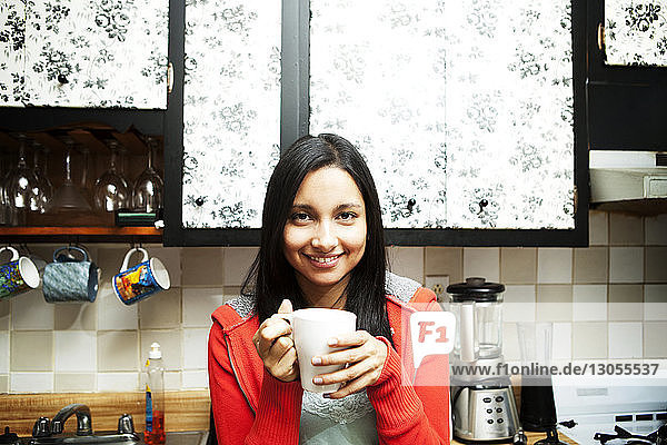 Portrait of happy young woman holding coffee cup in kitchen