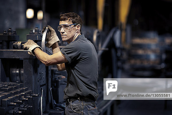 Worker looking away while standing by machinery in metal industry