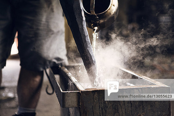 Mittelsektion eines Schmieds  der in einer Werkstatt Wasser auf einen heißen Stab gießt