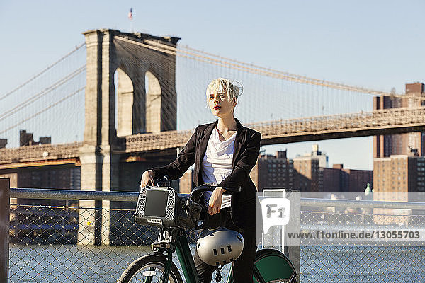 Frau steht mit Fahrrad und Helm gegen Brooklyn Bridge in der Stadt
