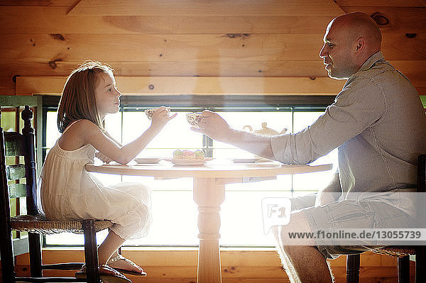 Vater und Tochter halten Teetassen  während sie am Tisch sitzen