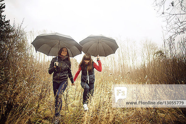 Freundinnen gehen mit Regenschirmen auf Grasfeld gegen den Himmel