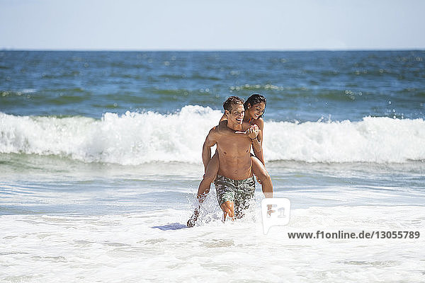 Mann nimmt am sonnigen Tag seine Freundin im Meer huckepack gegen den Himmel