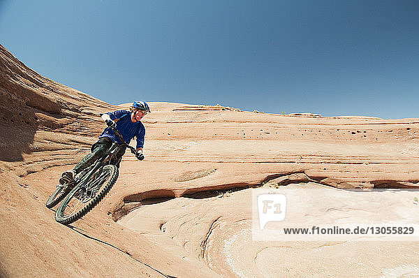 Man cycling on rock formation against clear blue sky