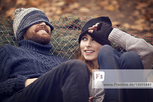 Woman looking at man wearing knit hat while leaning on Christmas Tree