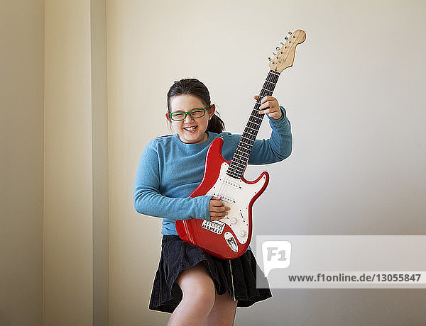 Fröhliches Mädchen spielt zu Hause Gitarre an der Wand