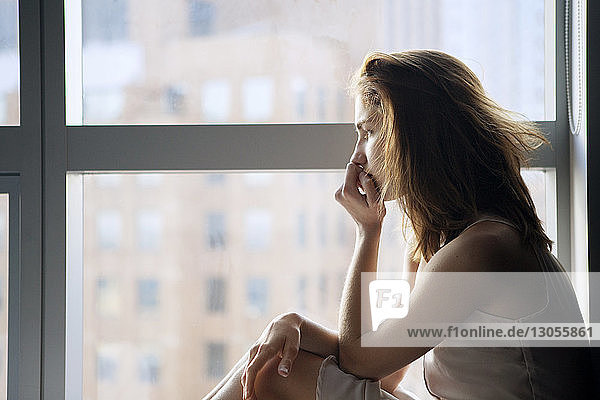 Seitenansicht einer nachdenklichen Frau am Fenster sitzend