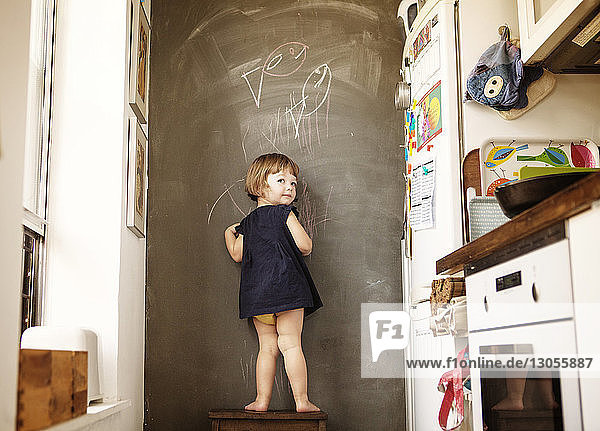 Rear view of girl writing on wall while standing on stool at home