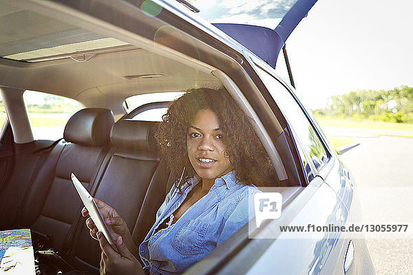Portrait of young woman using tablet computer while traveling in car