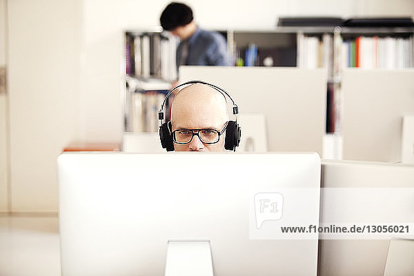 Geschäftsmann  der einen Computer benutzt  während er im Büro Kopfhörer trägt