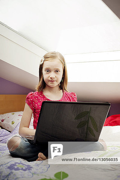 Portrait of girl sitting with laptop computer on bed at home