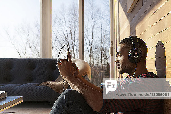 Mann hört Musik über Kopfhörer  während er zu Hause ein Smartphone in der Hand hält