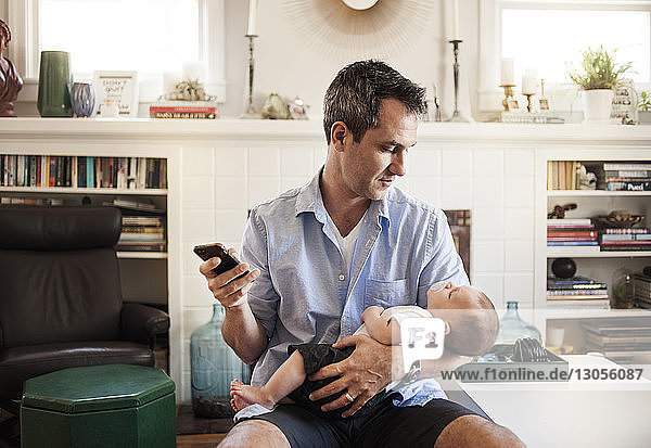 Man using mobile phone while looking at baby boy