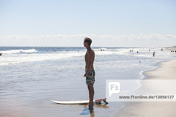 Man looking away while standing at shore with surfboard