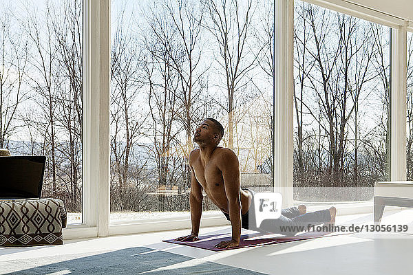 Junger Mann übt zu Hause nach oben gerichtete Hunde-Yoga-Position