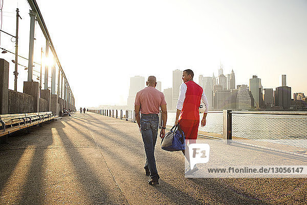 Rear view of father and son walking on promenade by East River in city