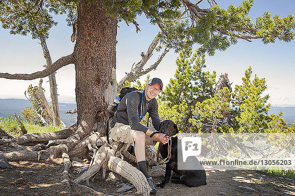 Portrait of smiling man sitting on roots by dog at field