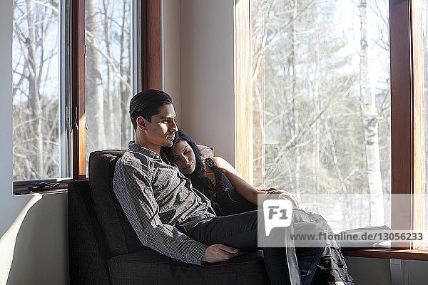Couple relaxing on chair by window at home