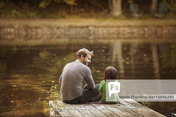 Rückansicht von Vater und Sohn auf einem Steg am See sitzend
