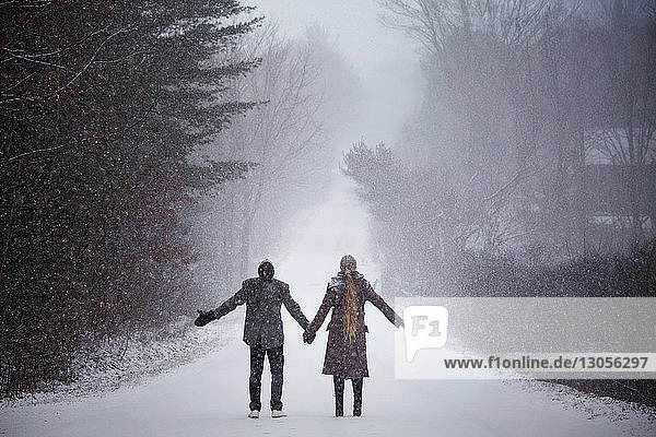 Couple holding hands while standing on snowy field during winter