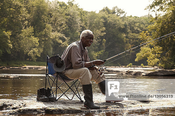 Happy man fishing while sitting by lake