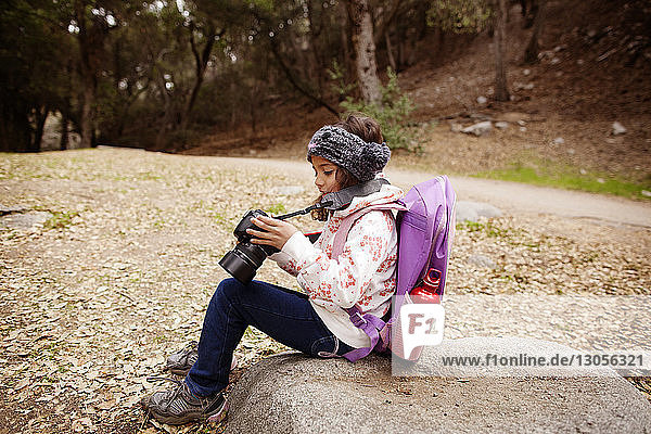 Mädchen benutzt Kamera  während sie auf einem Felsen im Feld sitzt